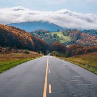 Mountain road surrounded by trees in fall colors and clouds