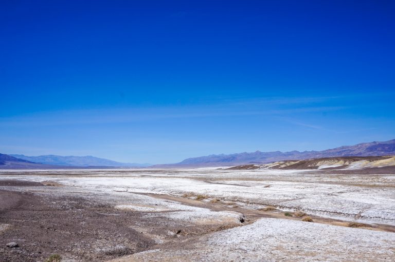 View of a desert landscape with a salt flat and mountains in the background, against a clear blue sky