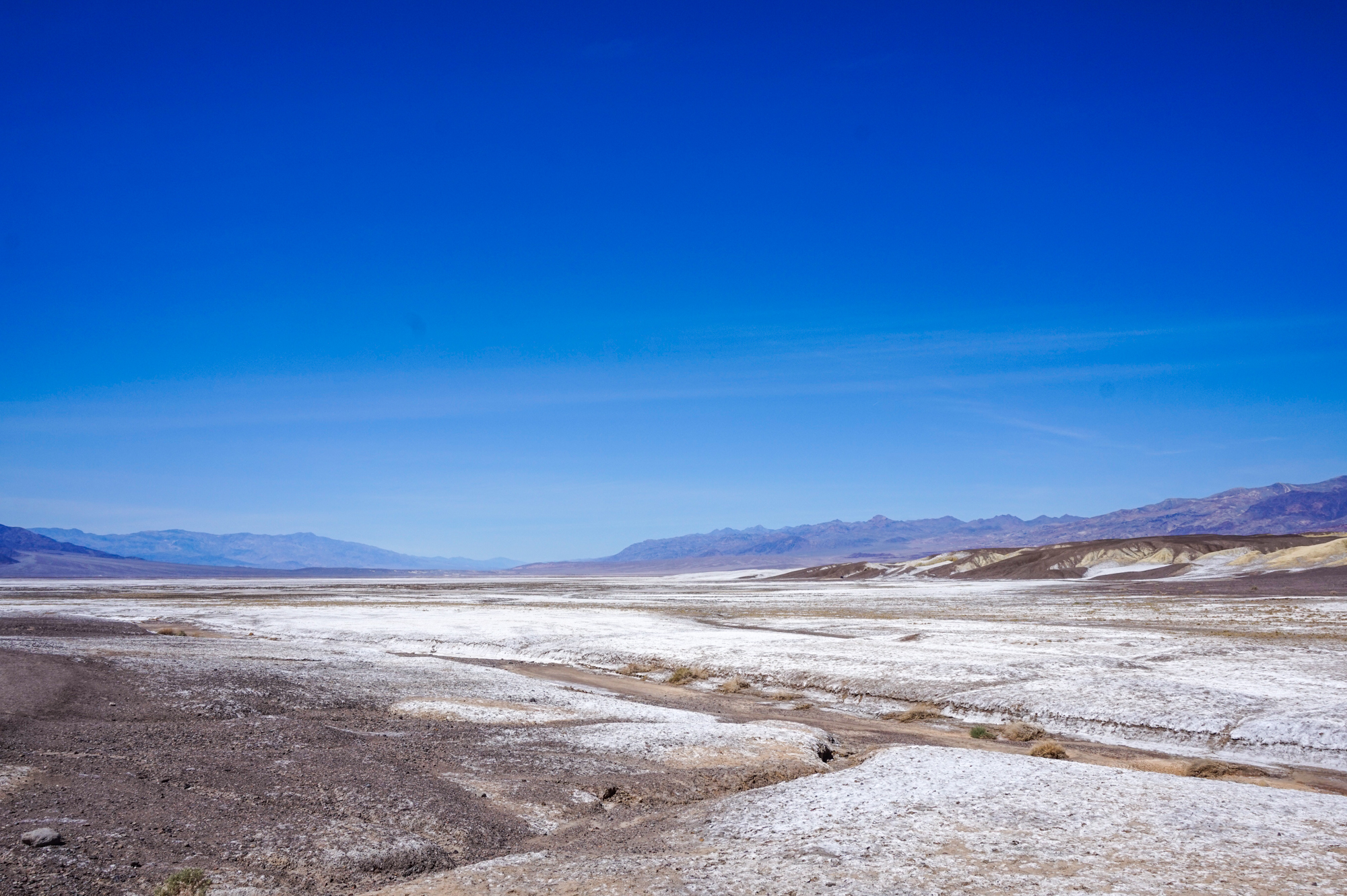 View of a desert landscape with a salt flat and mountains in the background, against a clear blue sky