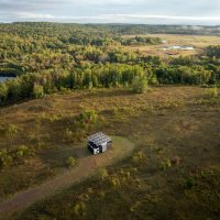 Aerial view of lush green landscape with a camping structure with big solar panels on the roof visible in the distance