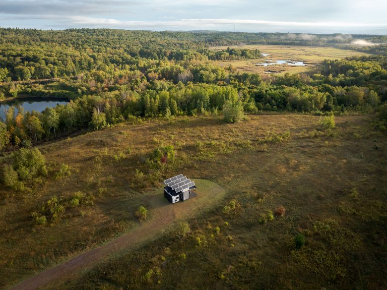 Aerial view of lush green landscape with a camping structure with big solar panels on the roof visible in the distance