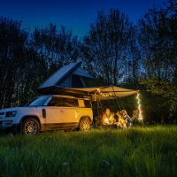 A car camping setup with a tent and campfire in a dark wooded area