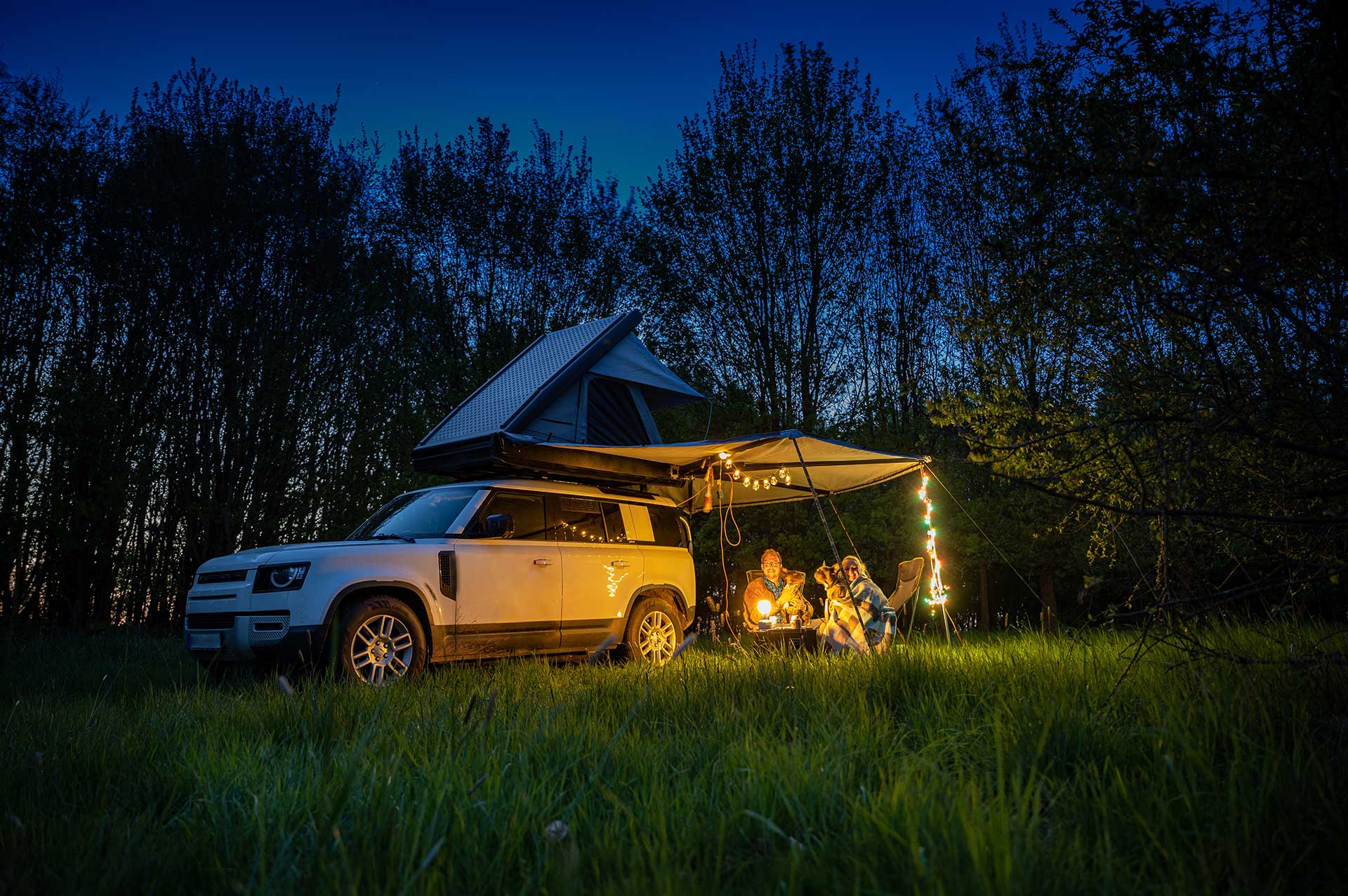 A car camping setup with a tent and campfire in a dark wooded area