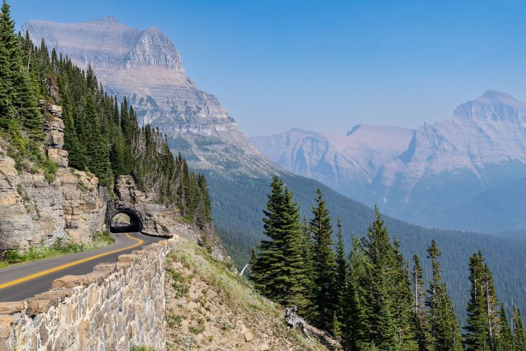 A scenic road with a tunnel and a drop-off into a mountain valley