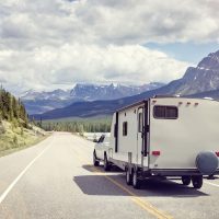 A truck pulling a travel trailer traveling along a scenic road surrounded by mountains