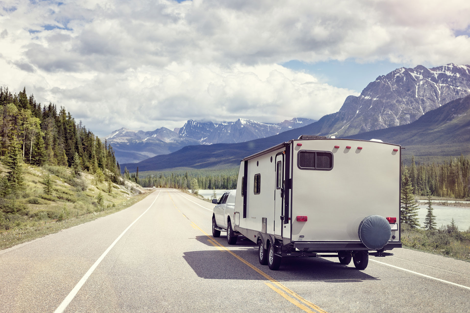 A truck pulling a travel trailer traveling along a scenic road surrounded by mountains
