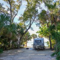 A trailer parked in a lush, foresty campsite with a water view