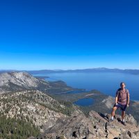 Man standing on a tall cliff with a lake behind him