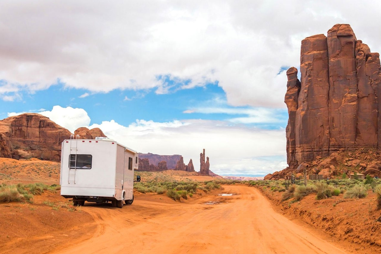 An RV parked on the side of a dirt road, surrounded by red sandstone rock formations