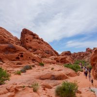 A line of people walking on a hiking trail through a red rock landscape